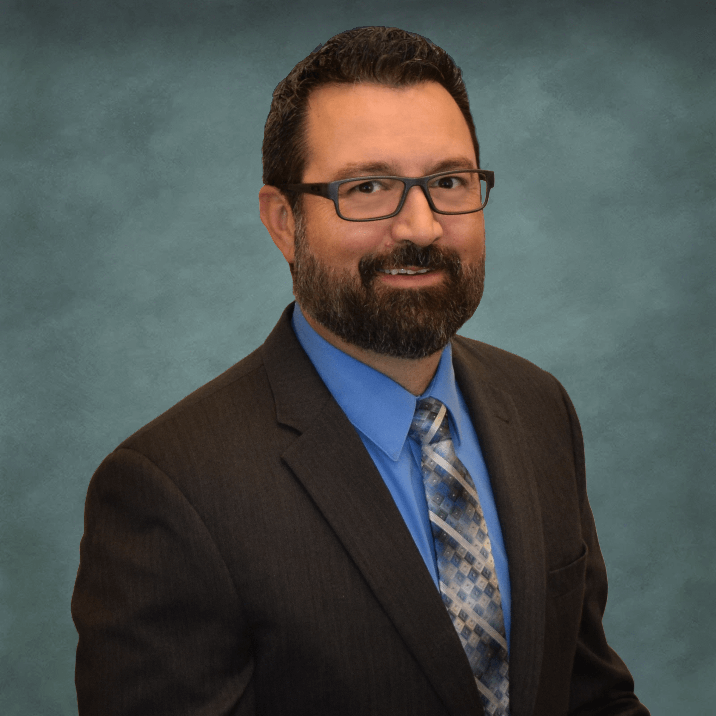 A professional headshot of Dr. Eric Torgerson, the owner and lead optometrist at Poudre Valley Eyecare, wearing a dark suit, blue shirt, and patterned tie against a greenish-grey background.